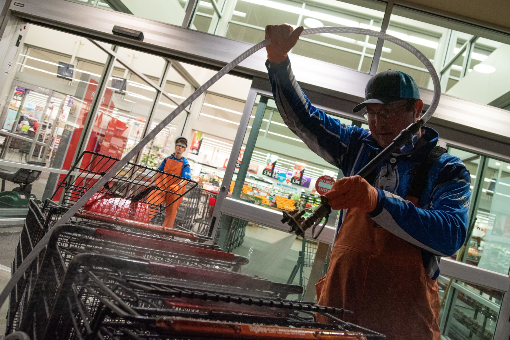Marty Osborn sanitizes down carts outside of HyVee while Seth Trojcak gathers up dirty carts inside that need to be sanitized.